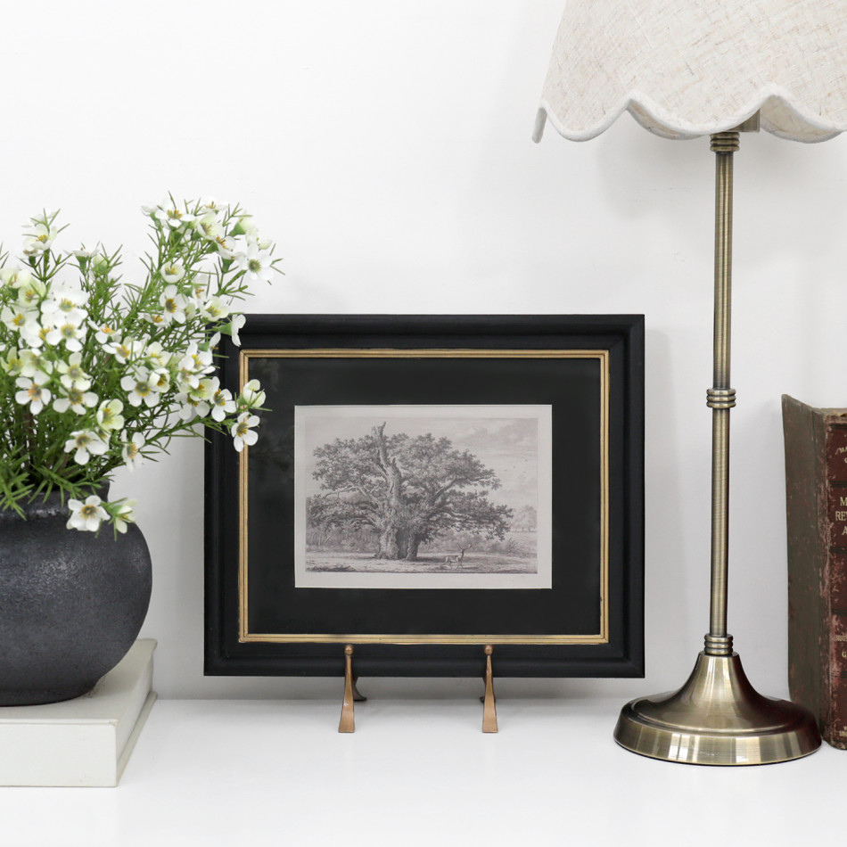 Sandhurst framed tree print styled on a white console with flowers, a brass lamp and vintage books.