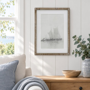 Falmouth Harbour II framed print above a timber cabinet beside a cream armchair and a vase of eucalyptus