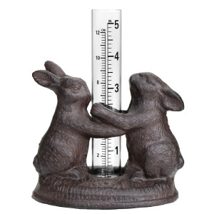 Two brown cast iron rabbits holding a glass rain gauge with centimetre and inch markings on a white background