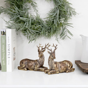 Antique gold reindeer pair styled on a white shelf with books, a green wreath and a white jug