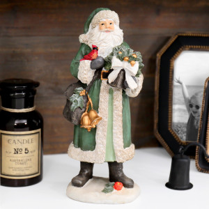 Green St Nicholas figurine with gold bells, a red bird and festive greenery displayed beside a candle and photo frame