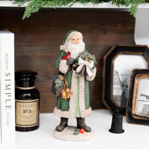 Green St Nicholas Christmas decoration on a white shelf with books, a candle and family photo frames beneath greenery