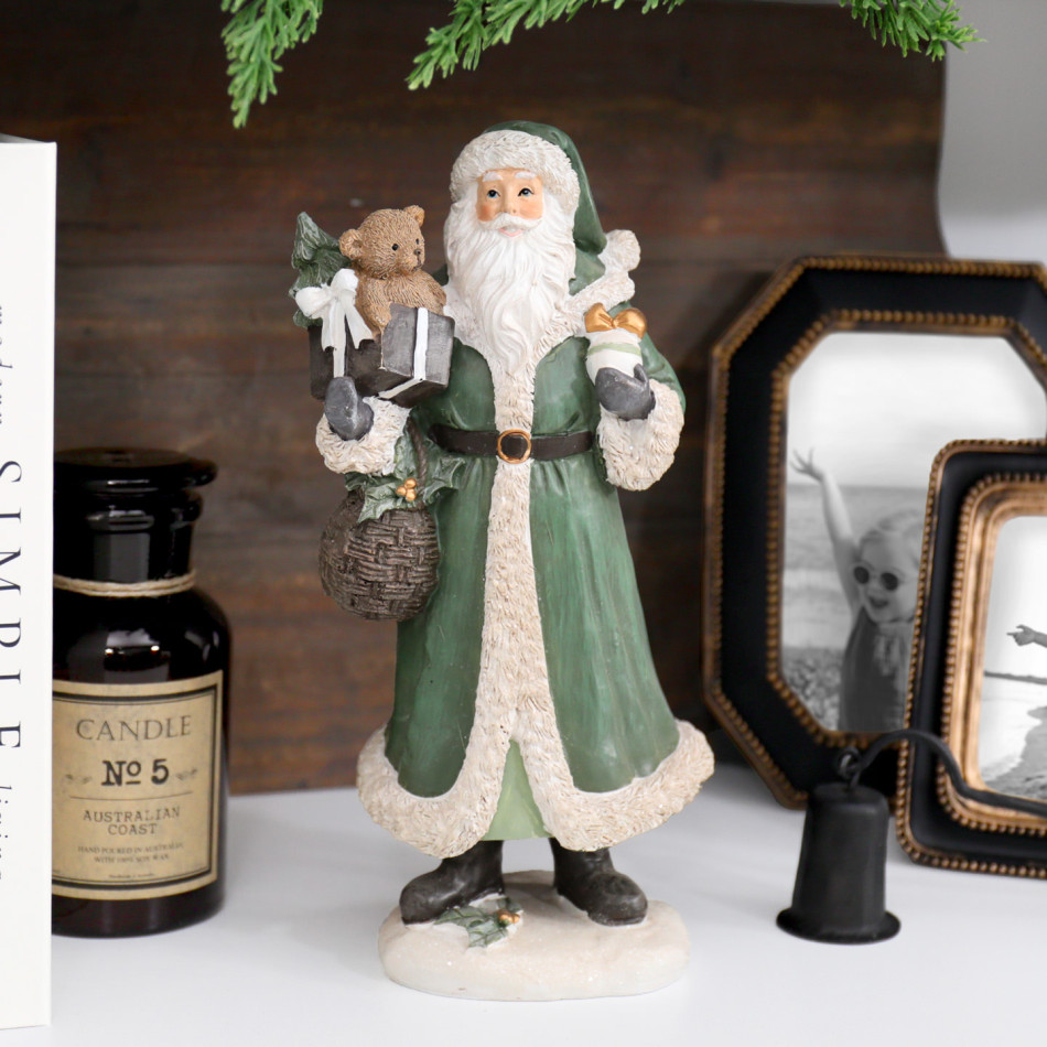 Green St Nicholas figurine carrying a teddy bear and presents, displayed beside a candle and dark photo frames