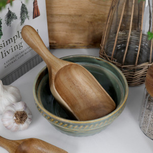 Large acacia wood scoop resting inside a green ceramic bowl in a styled kitchen setting