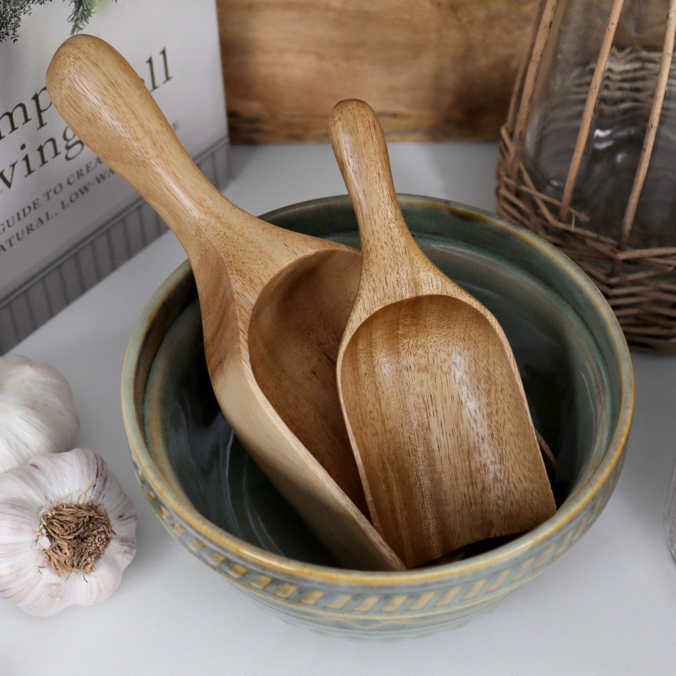 Large and small acacia wood scoops displayed together in a green ceramic bowl