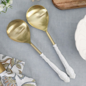 Pair of gold-toned serving spoons with decorative white enamel handles styled on blue table linen