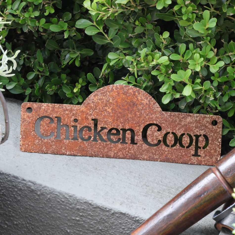 Rusty steel Chicken Coop sign with cutout lettering, styled beside garden tools and leafy plants
