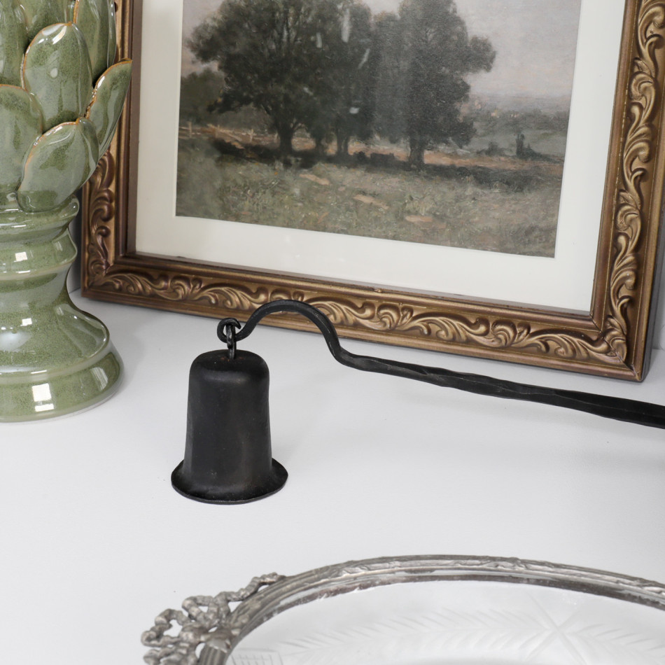 Black hand-forged iron candle snuffer styled beside an ornate framed artwork
