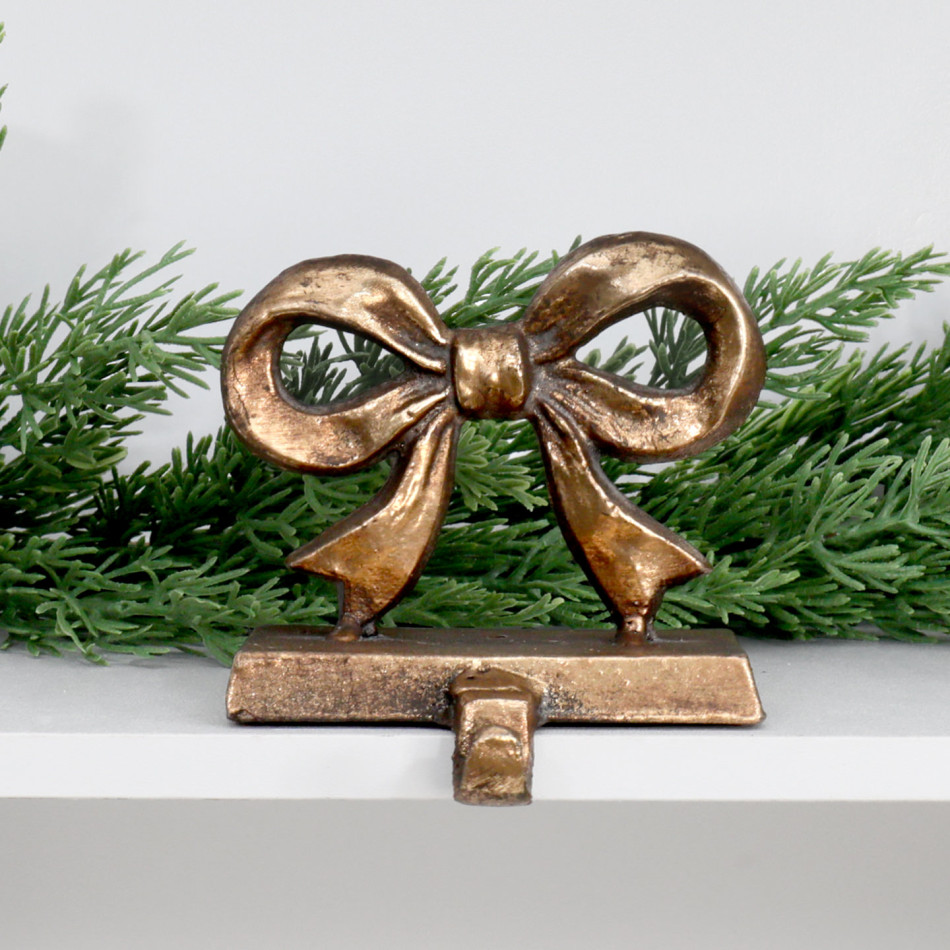 Clara gold bow stocking hook displayed on a white shelf beneath Christmas greenery.