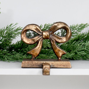 Clara gold bow stocking hook displayed on a white shelf beneath Christmas greenery.