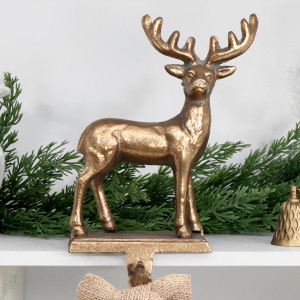 Gold reindeer stocking hook on a white shelf with festive greenery and a natural fabric bow hanging below