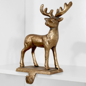 Angled view of the cast iron gold reindeer stocking hook resting over the edge of a white shelf