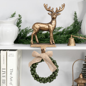 Dancer gold reindeer hook holding a green bell wreath beneath a shelf decorated with greenery and white ceramics
