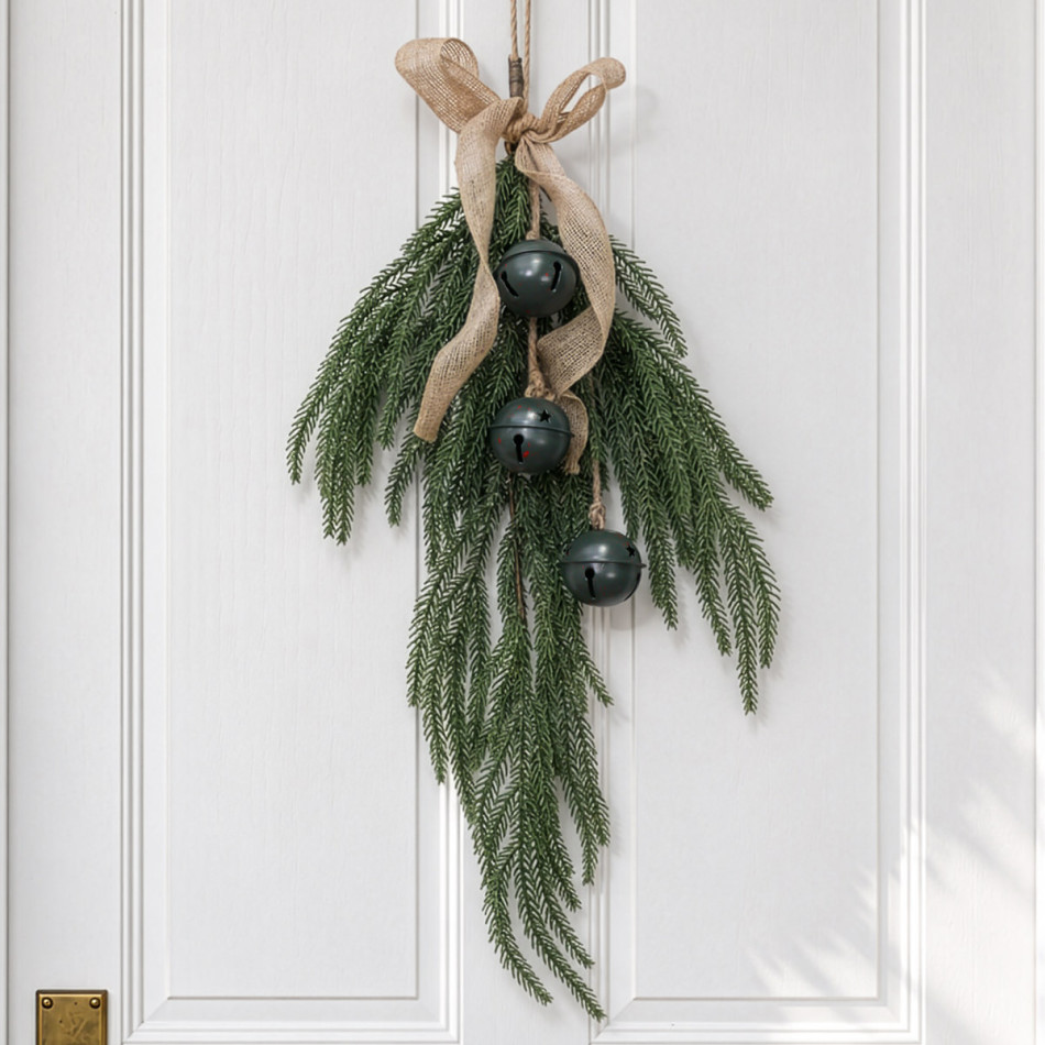 Glad Tidings Christmas swag with cascading green foliage, three dark green metal bells and a hessian bow against white panelling.