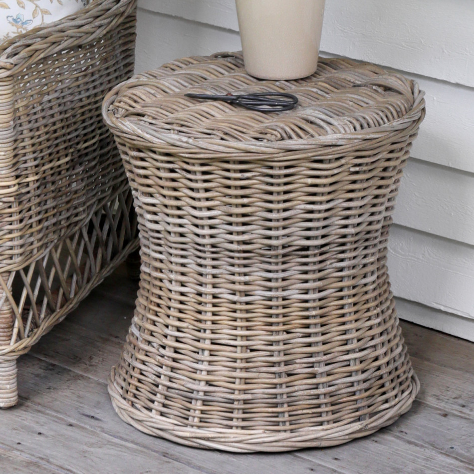Round antique-grey rattan side table with woven top styled beside a cane armchair