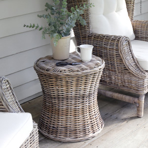 Round woven cane side table styled with a potted plant and cup between armchairs