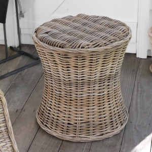 Freestanding round rattan side table with curved hourglass shape on a wooden floor