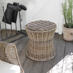 Round rattan side table on a covered verandah beside a chair and potted plant