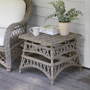 Antique-grey cane side table styled with a plant, books and cup between rattan chairs