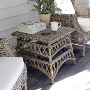 Square woven rattan side table positioned between two cream-cushioned cane armchairs