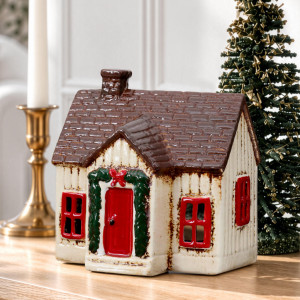 Close-up of ceramic Christmas cottage with a red door, green garland and brown tiled-look roof