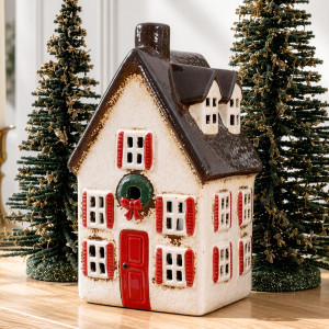 Close-up of tall ceramic Christmas house with red shutters, a green wreath and brown roof with dormer windows