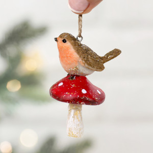Close-up of glitter-accented robin on a red spotted toadstool, held by its hanging loop against blurred tree lights