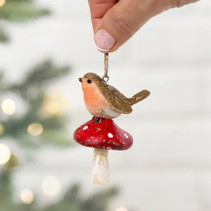 Resin robin on a red toadstool held in front of a softly blurred Christmas tree with warm lights