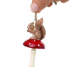 Hand holding a squirrel on toadstool ornament by its twine hanging loop against a white background