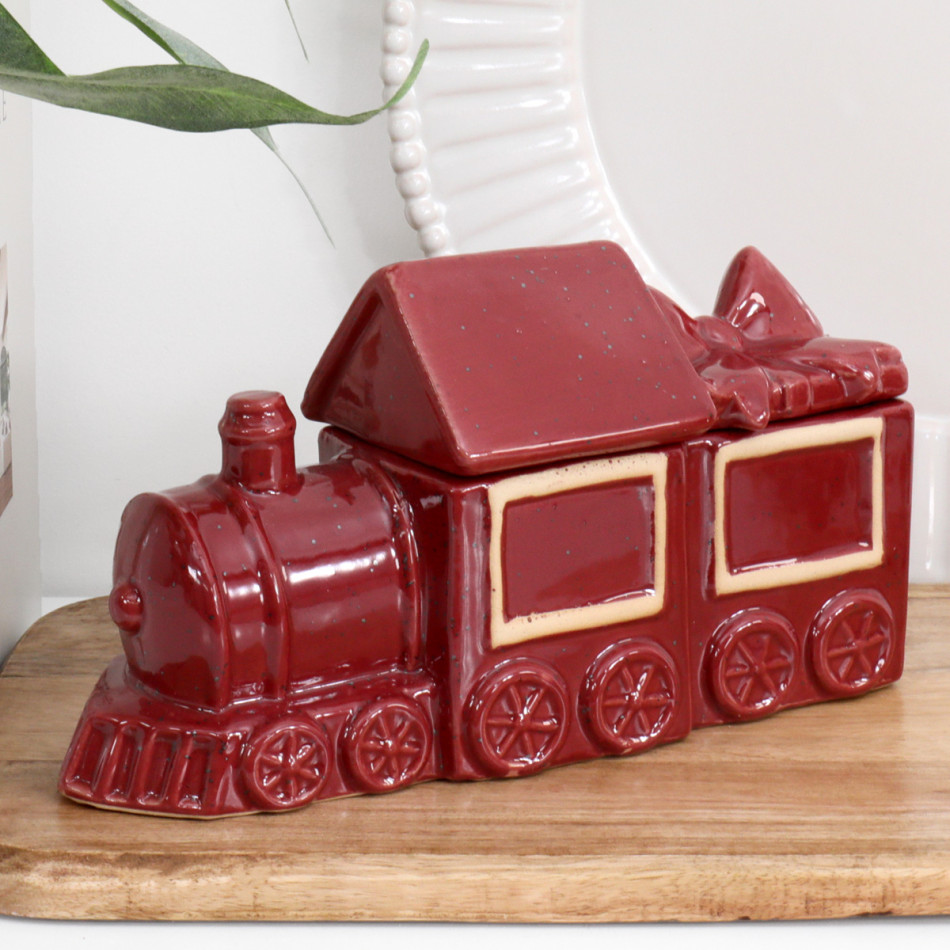 Hollybrook red ceramic Christmas train trinket box with cream panel outlines and a bow-topped lid on a wooden board.