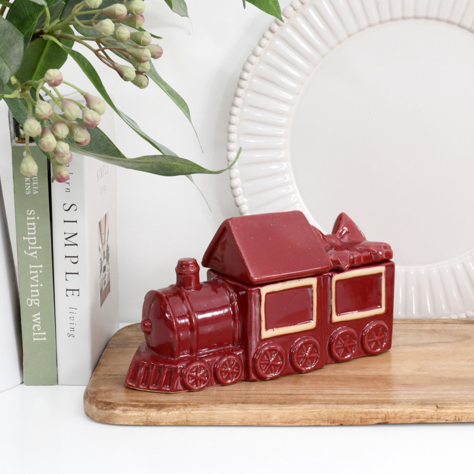 Hollybrook red Christmas train box styled on a wooden board beside books, leafy stems and a white decorative plate.