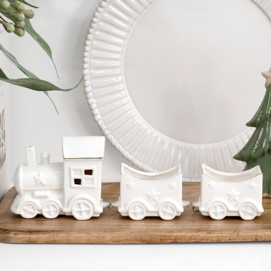 White ceramic Christmas locomotive and two star-decorated carriages on a wooden board in front of a white plate.