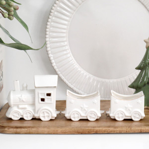 White ceramic Christmas locomotive and two star-decorated carriages on a wooden board in front of a white plate.