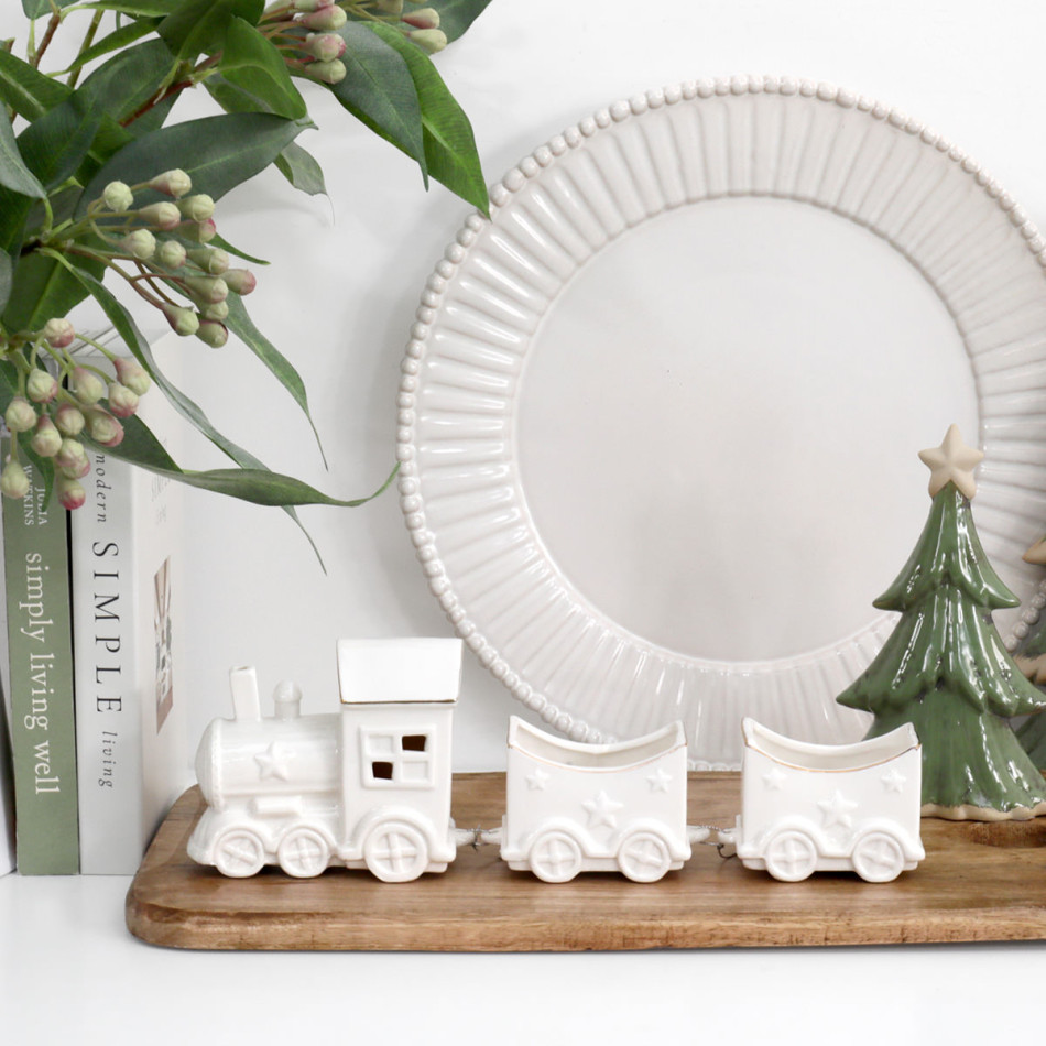 North Pole white ceramic Christmas train styled with books, leafy stems, a white decorative plate and a green ceramic tree.