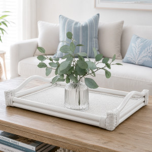 White rattan tray with raised handles styled on a timber coffee table with a glass vase and foliage