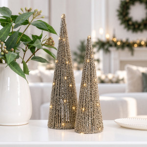 Gold beaded LED Christmas trees beside a white vase of greenery in a festive living room