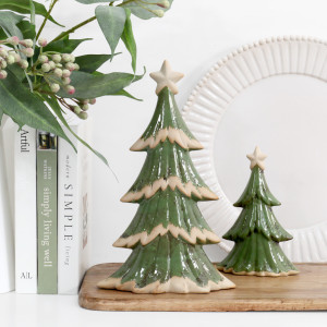 Large and small Forest Wishes ceramic Christmas trees on a wooden board with leafy stems, books and a white decorative plate.