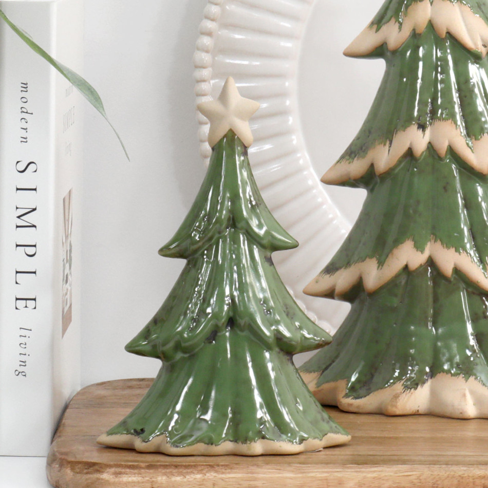 Small green ceramic Christmas tree with a cream star on a wooden board beside books, a white plate and the larger tree.