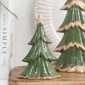 Small green ceramic Christmas tree with a cream star on a wooden board beside books, a white plate and the larger tree.