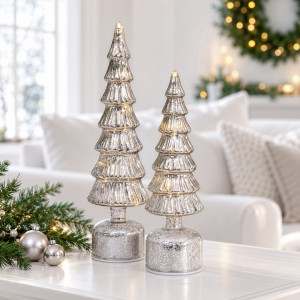 Large and small silver light-up Christmas trees on a white table in a softly styled living room