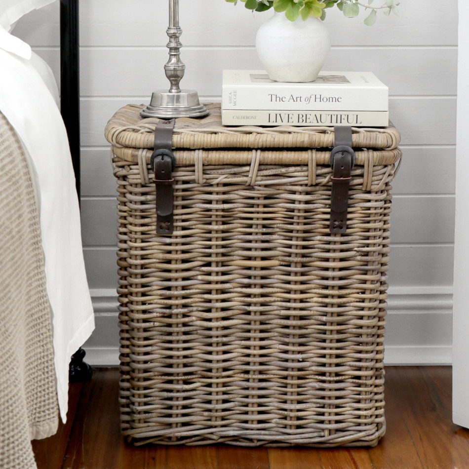 Grey-brown woven rattan trunk with leather straps styled beside a bed
