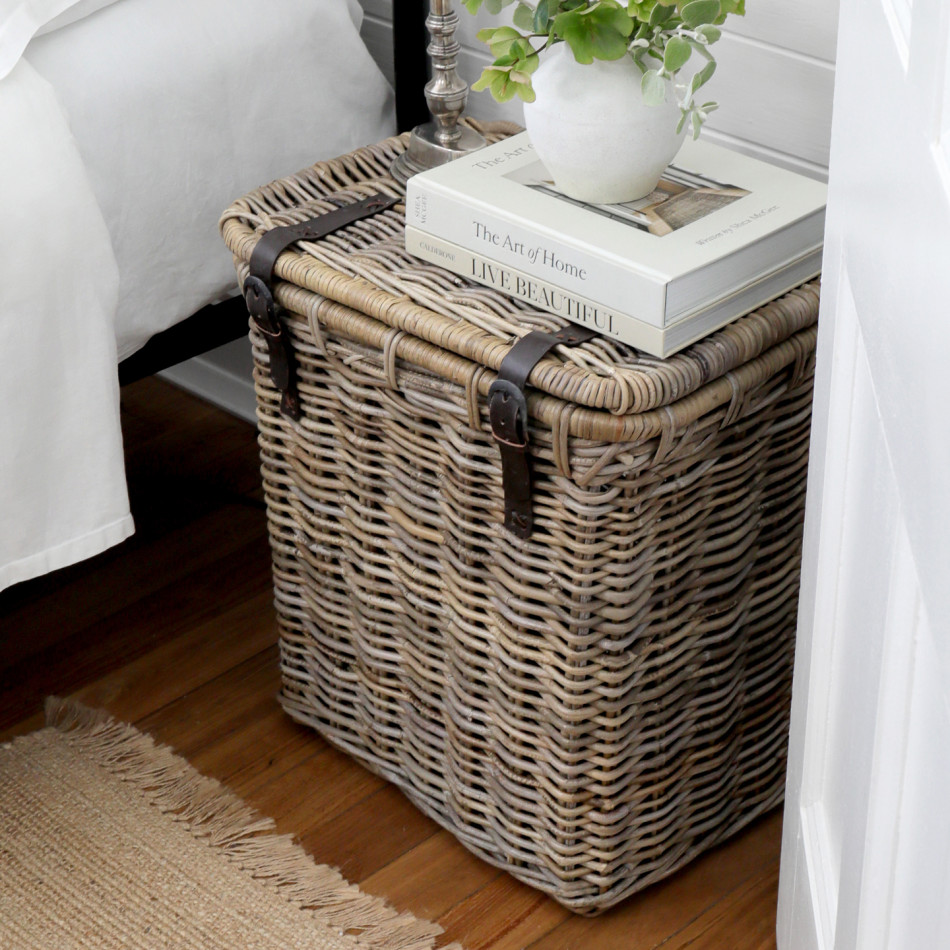 Angled view of rattan bedside trunk topped with books and a white vase