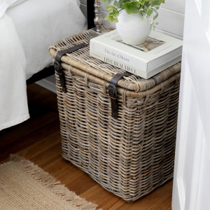 Angled view of rattan bedside trunk topped with books and a white vase