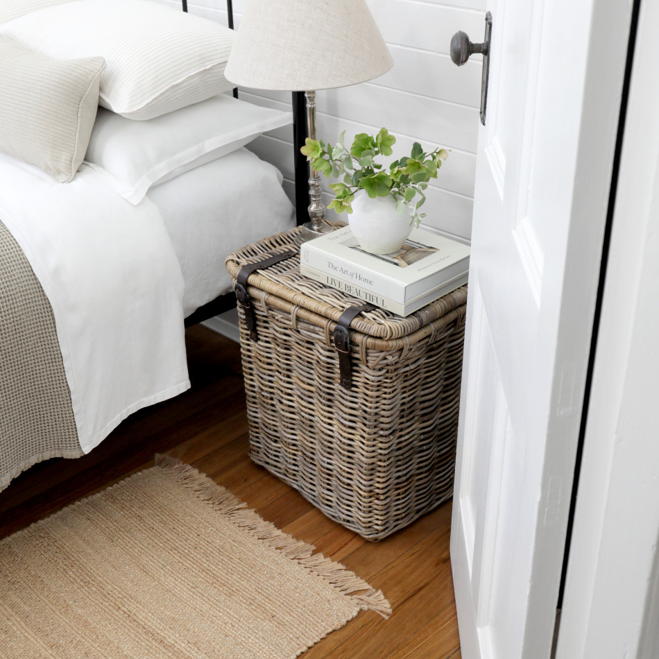 Rattan storage trunk used as a bedside table with a lamp, books and vase