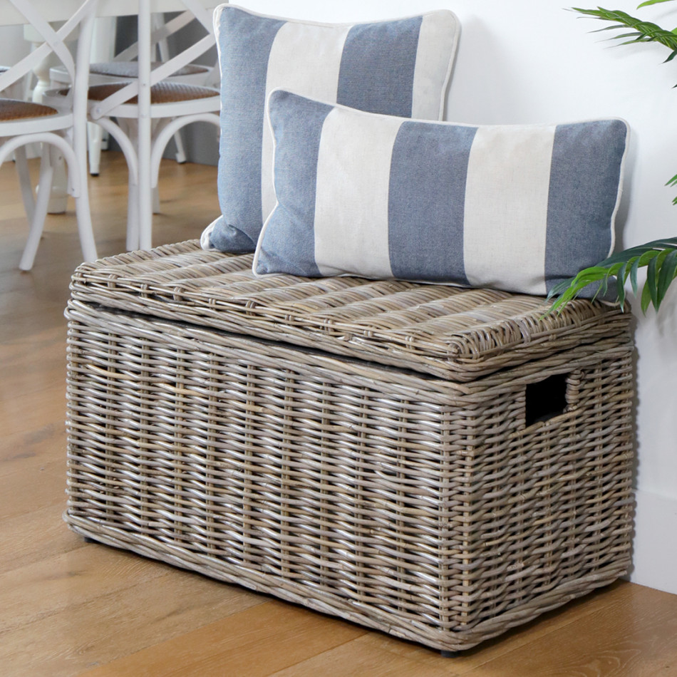 Antique-grey rattan storage trunk with blue and white cushions arranged on its closed lid