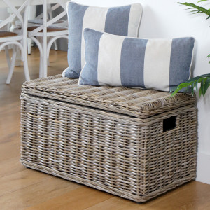 Antique-grey rattan storage trunk with blue and white cushions arranged on its closed lid