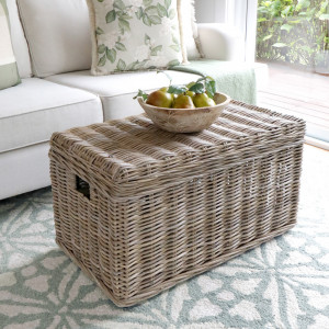 Antique-grey rattan trunk used as a living room table with a bowl on its woven lid
