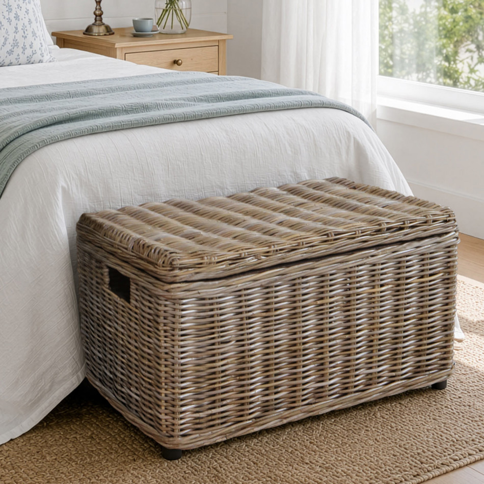 Closed Oliver rattan storage trunk positioned beside a bed on a wooden floor
