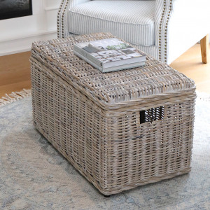Greywash rattan storage trunk with a closed woven lid beside a blue striped armchair
