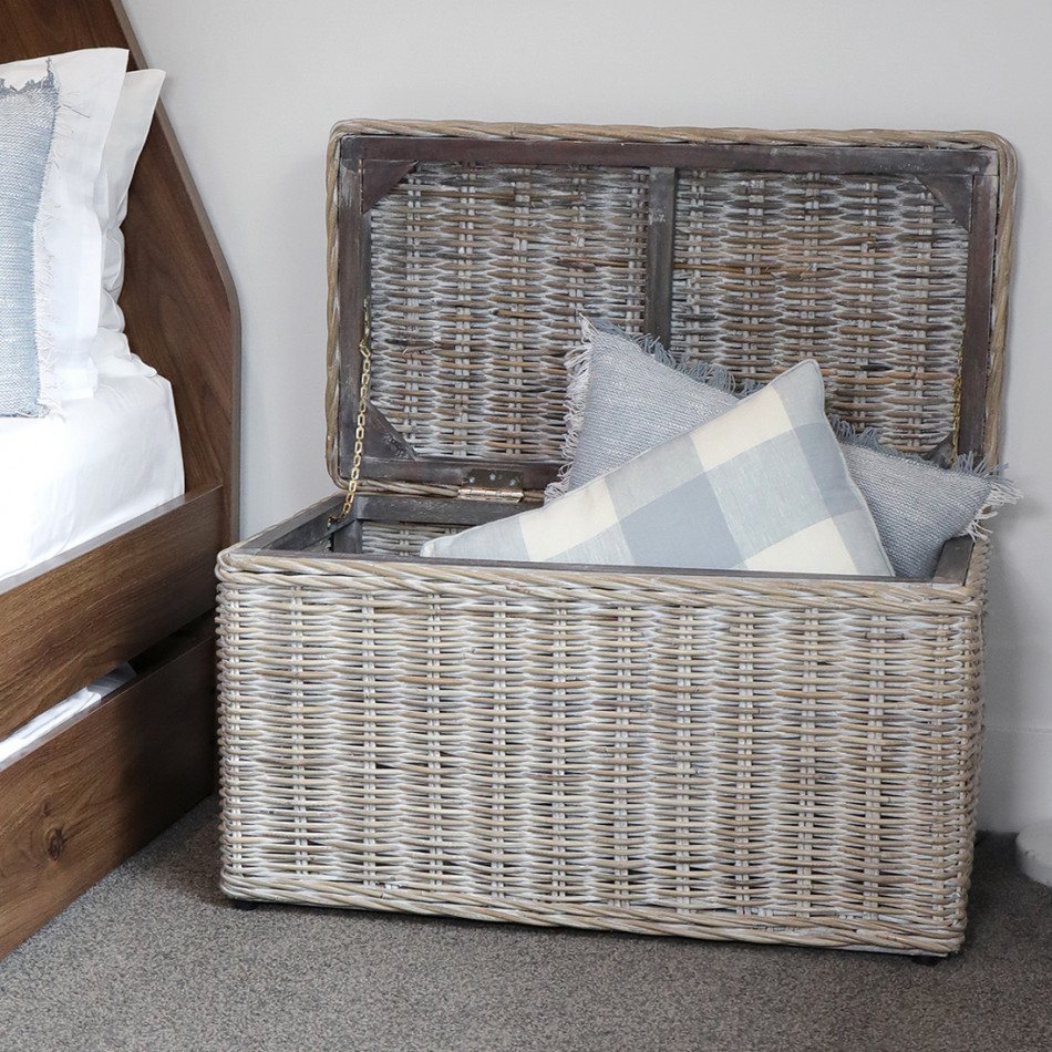 Greywash rattan storage trunk beside a bed with its hinged lid open